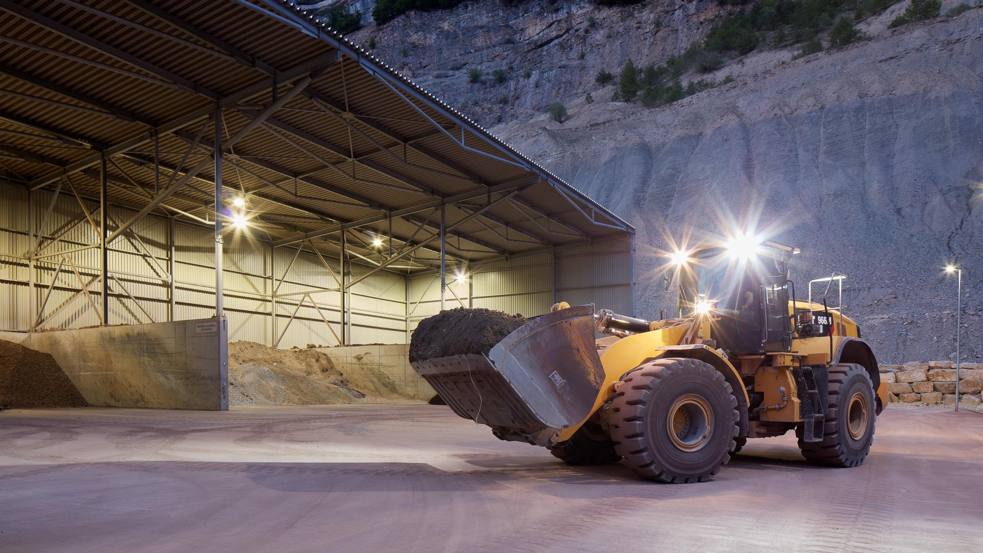 Ein Bagger steht vor einer Halle in einer Kiesgrube. Das Bild entstand am Abend bei Dämmerung.