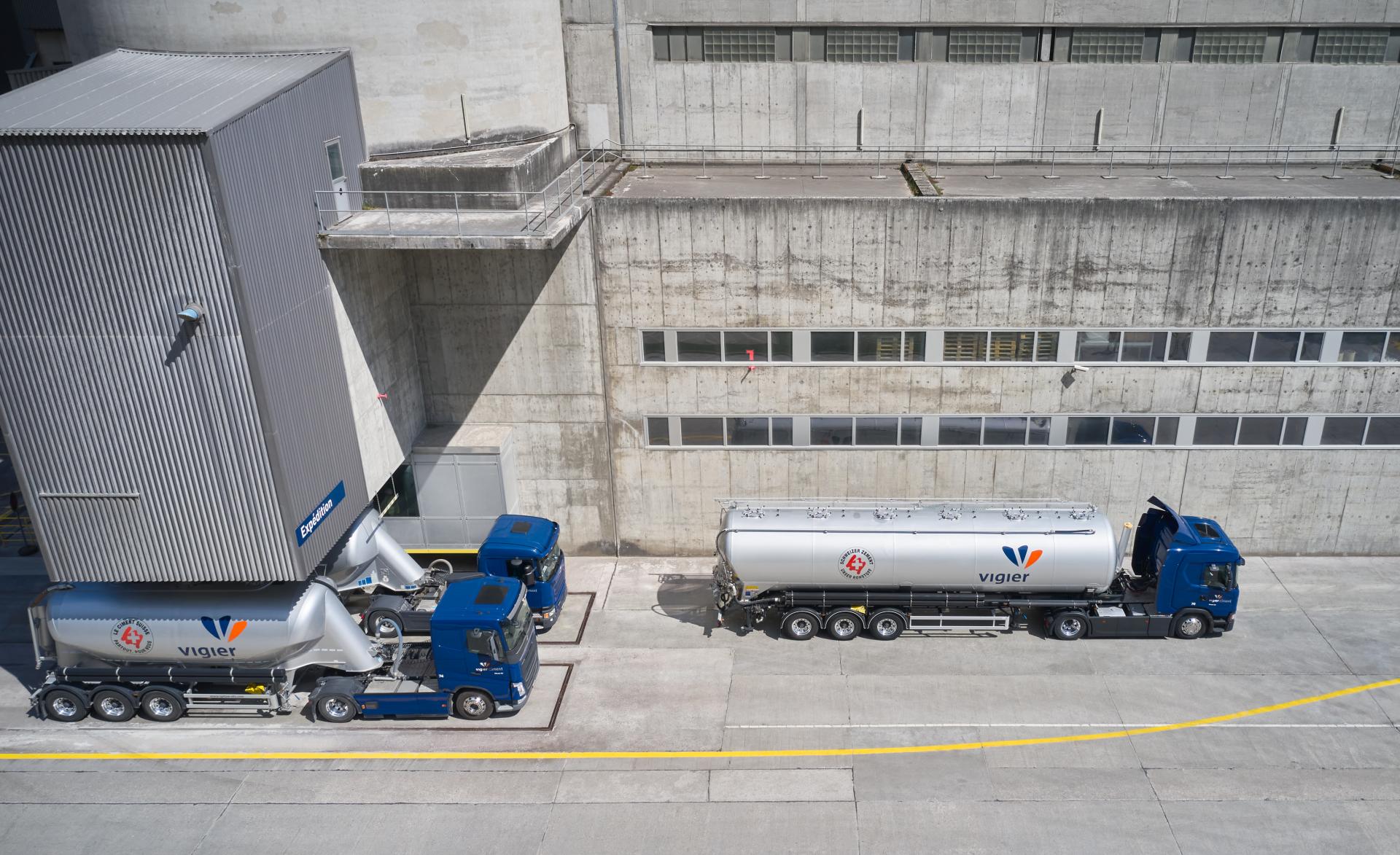 Mehrere Blau-Silberne Lastwagen von Vigier werden mit Zement beladen.