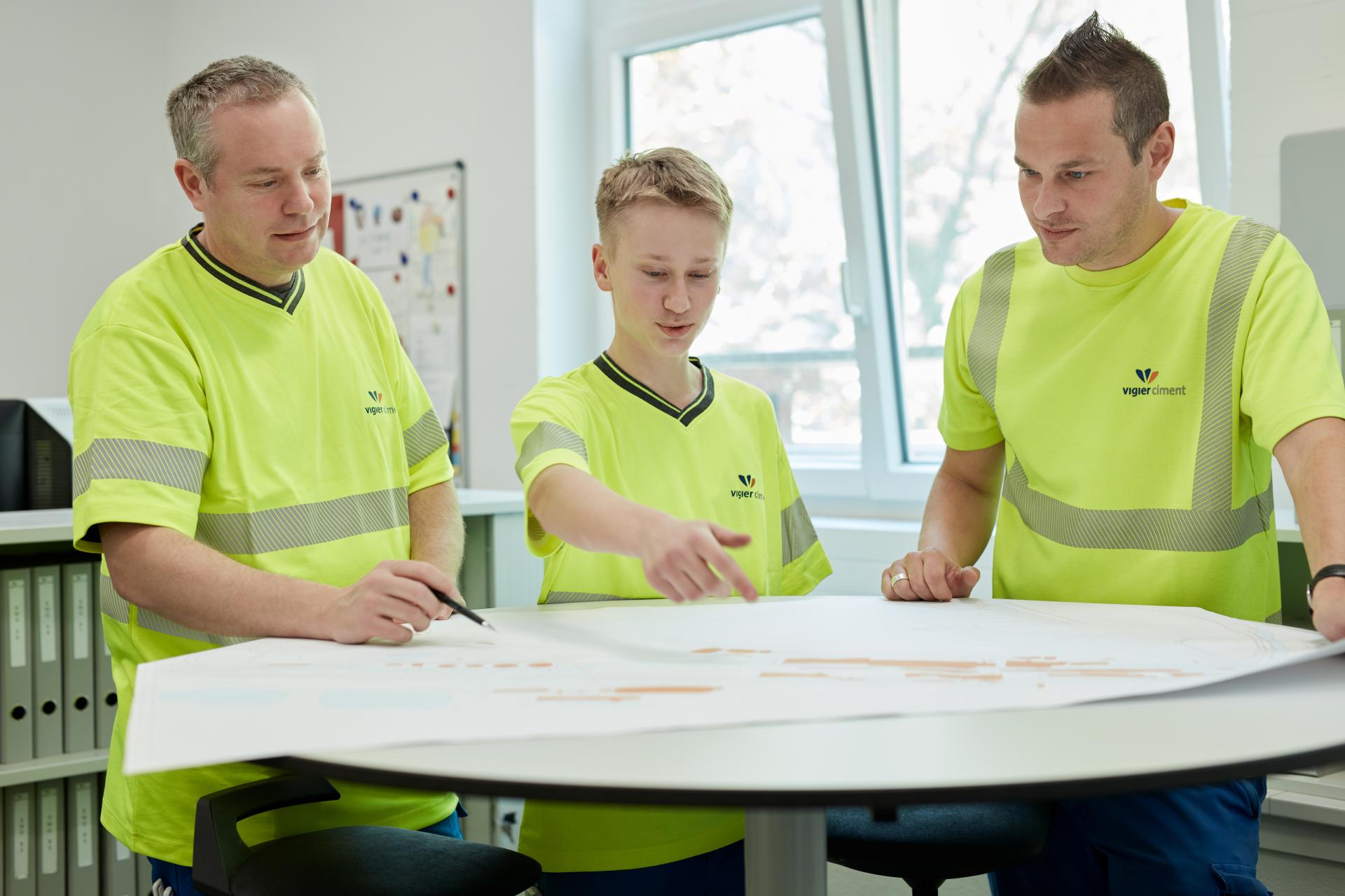 Zwei Mitarbeiter in Leuchtweste erklären einem Lehrling