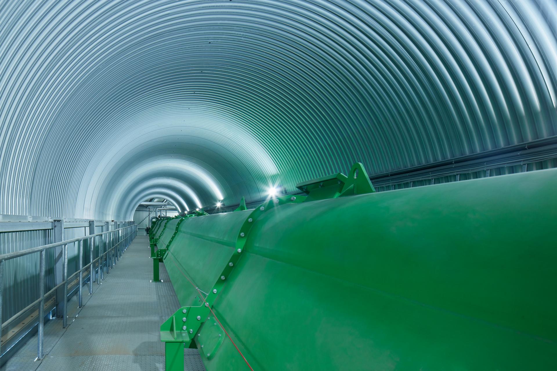 Eine grüne grosse Stahlröhre in einem runden Wellblech-Tunnel